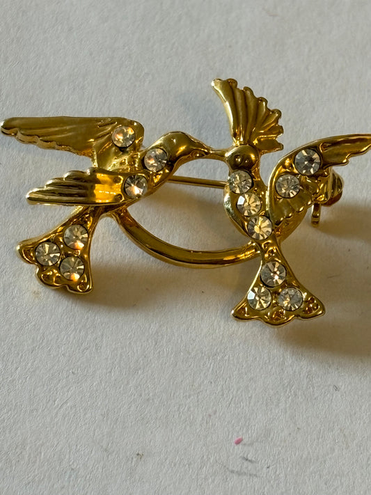 Bright gold metal brooch of two birds with diamantes