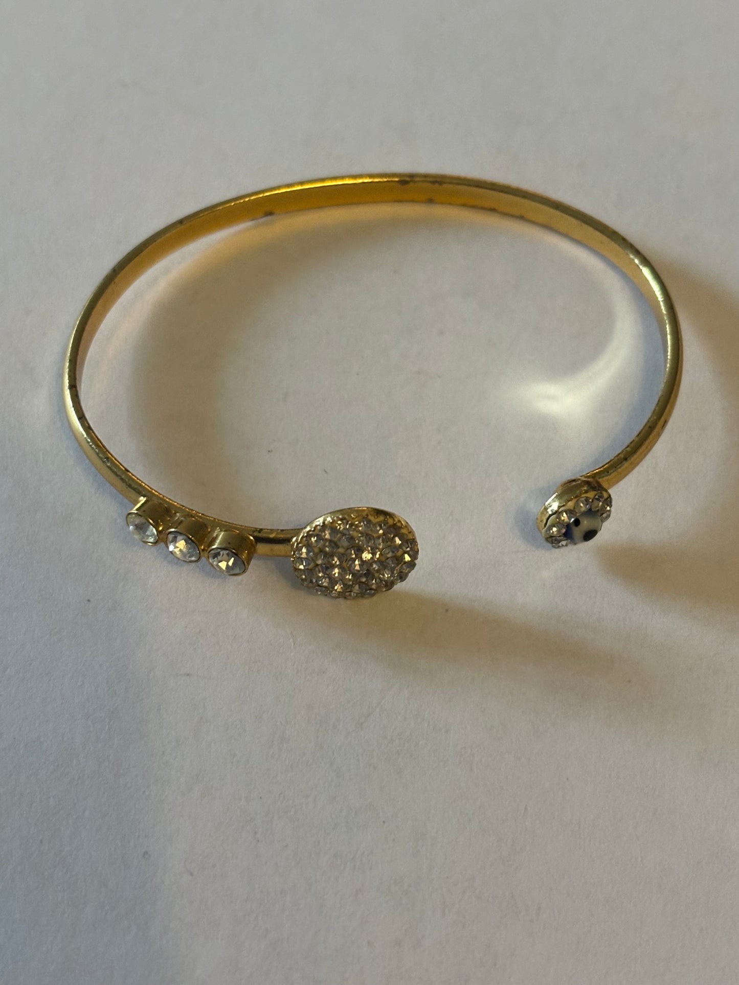 Gold metal bangle with clusters of white stones and blue bead