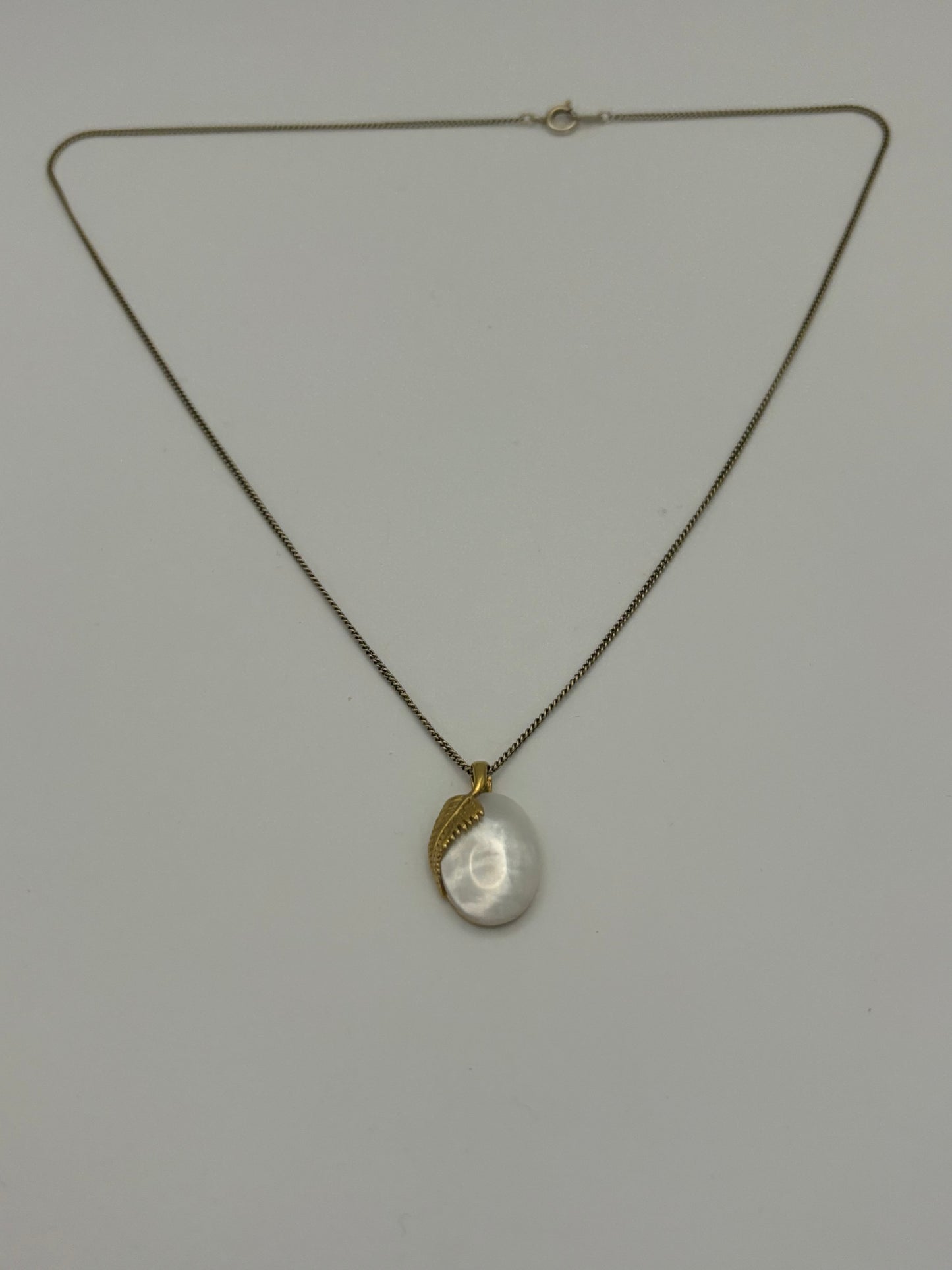 Gold metal chain necklace with oval pearlescent stone pendant with overlaid fern