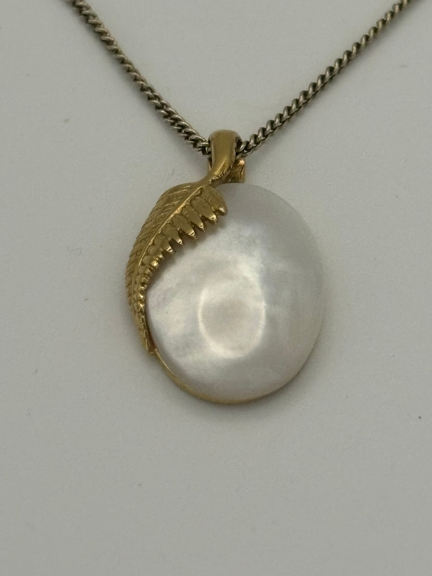 Gold metal chain necklace with oval pearlescent stone pendant with overlaid fern