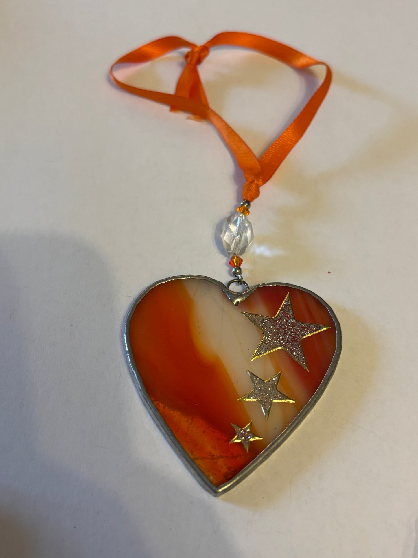 Silver metal heart ornament with orange filling and ribbon with stars