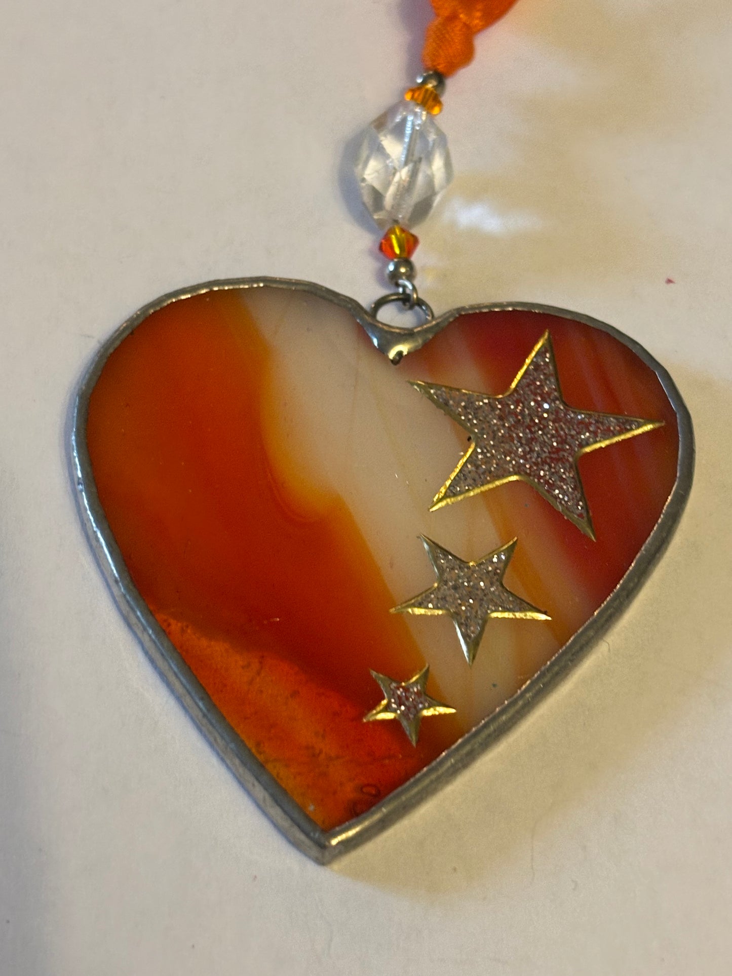 Silver metal heart ornament with orange filling and ribbon with stars