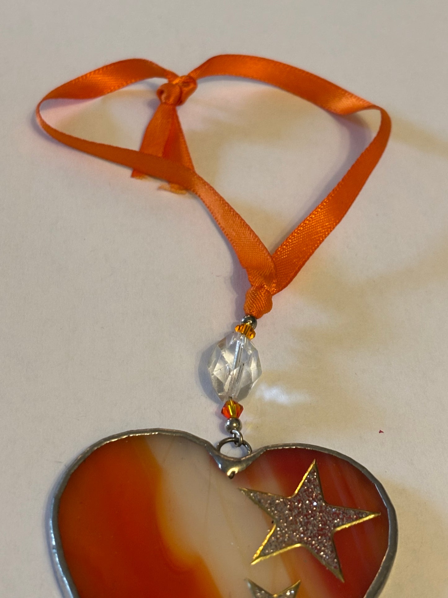 Silver metal heart ornament with orange filling and ribbon with stars