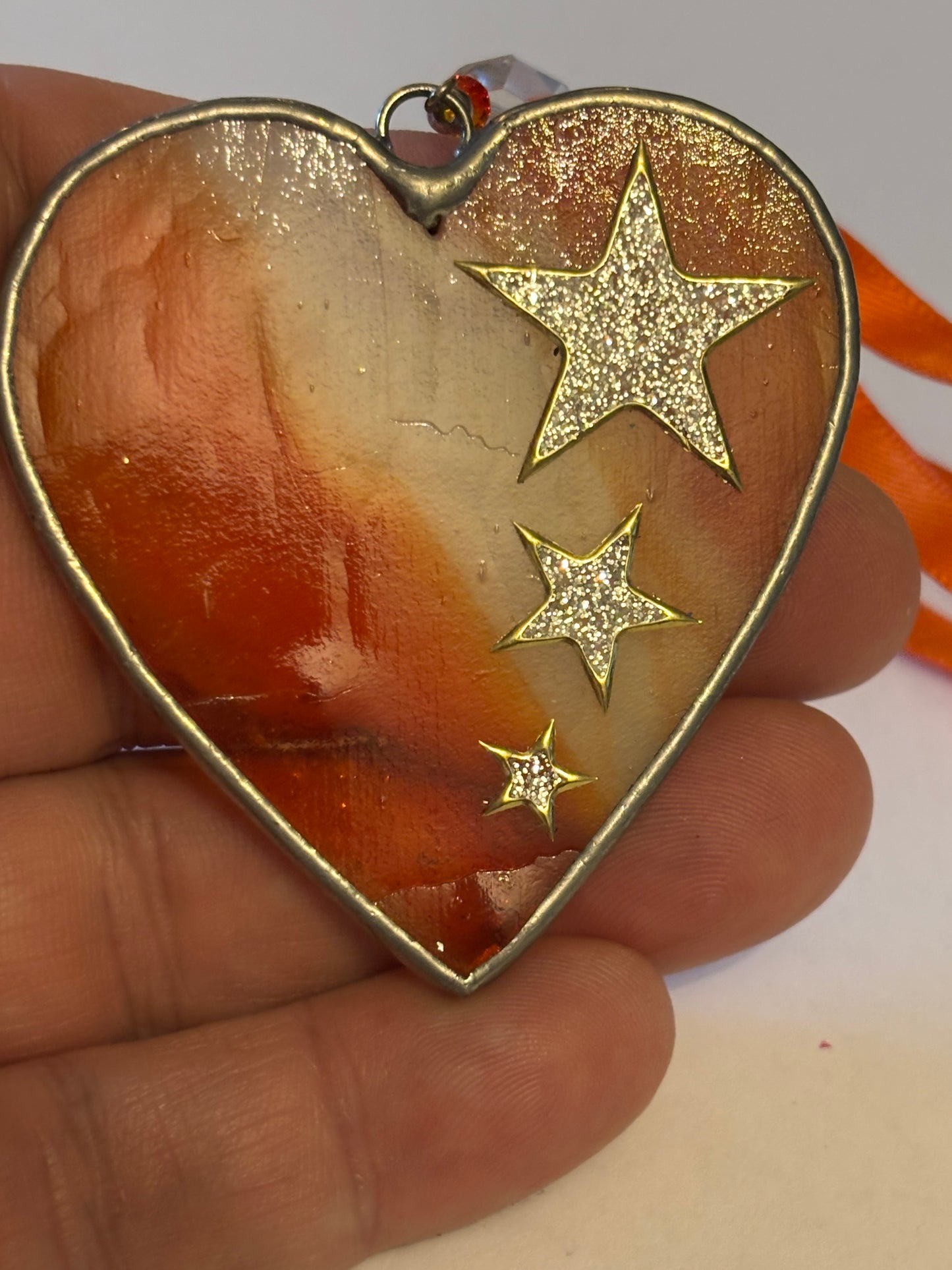 Silver metal heart ornament with orange filling and ribbon with stars