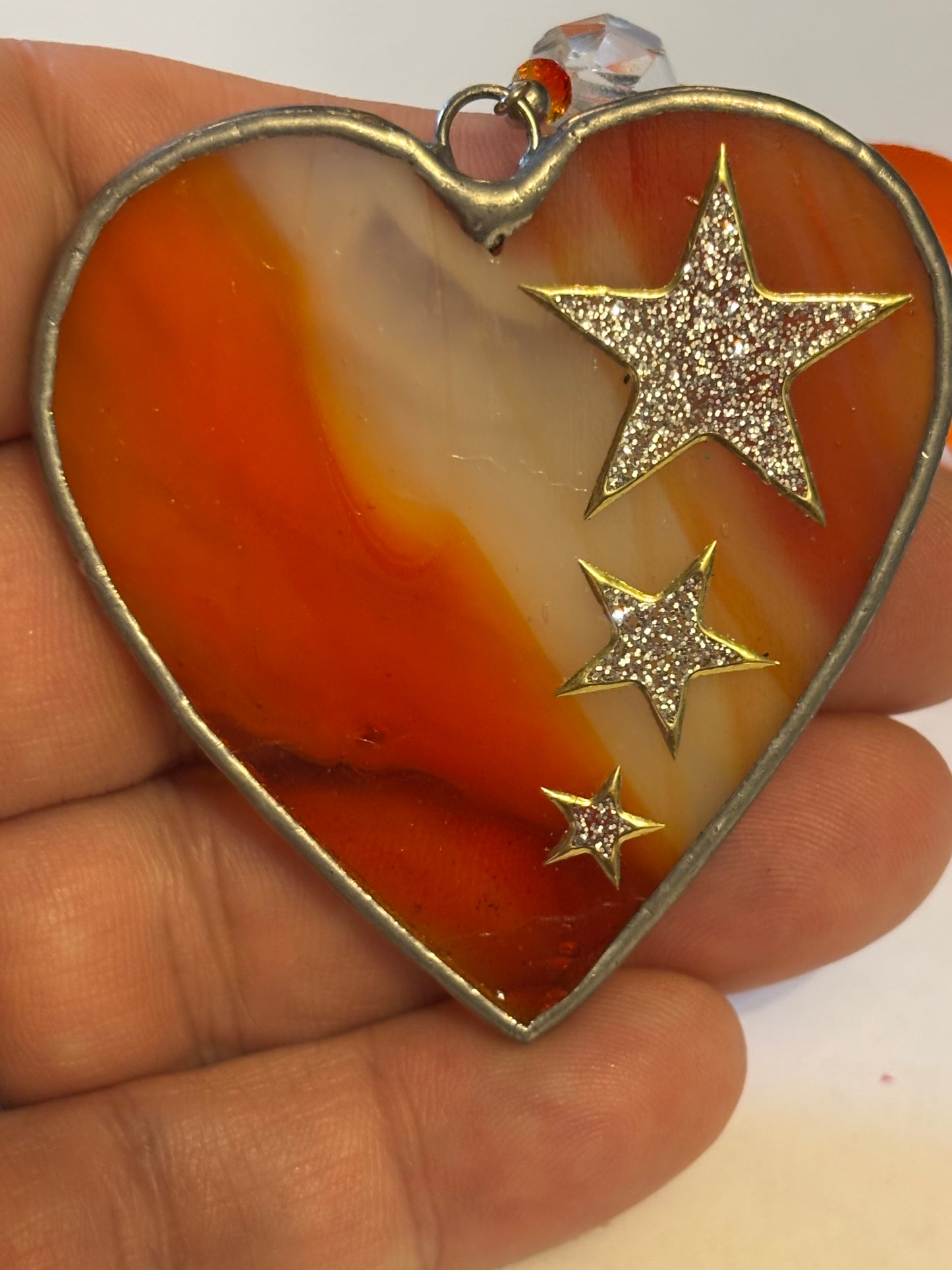 Silver metal heart ornament with orange filling and ribbon with stars